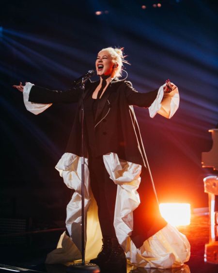 Christina Aguilera in a black dress singing at a concert.